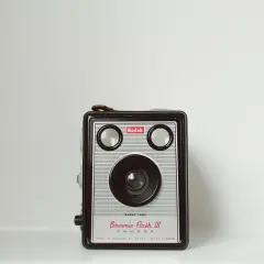 Kultowy aparat Kodak Brownie Flash III, symbol historii aparatu fotograficznego, z charakterystycznym obiektywem i dwoma wizjerami.