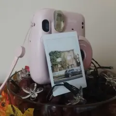 Różowy Instax Mini 11 zrobiony do robienia zdjęć, z wydrukowanym zdjęciem domu i samochodu.
