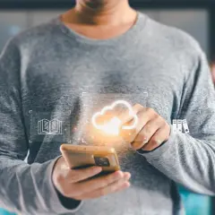Osoba trzymająca smartfon z ikonami chmury, książki i folderów.