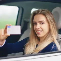 Uśmiechnięta młoda kobieta w samochodzie pokazuje swoje nowe prawo jazdy. Zdjęcie do prawa jazdy uszy są widoczne.