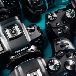 Zbliżenie na kilka aparatów cyfrowych marek Nikon, Canon i Sony. Widać ich detale, pokrętła i napisy. To jakby pierwszy aparat każdego z nich.