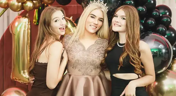 Trzy uśmiechnięte dziewczyny na 18. urodzinach, otoczone złotymi i czarnymi balonami. Zastanawiasz się, ile kosztuje fotograf na 18.?
