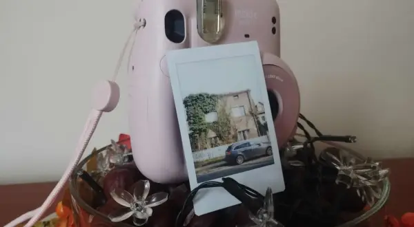 Różowy Instax Mini 11 zrobiony do robienia zdjęć, z wydrukowanym zdjęciem domu i samochodu.