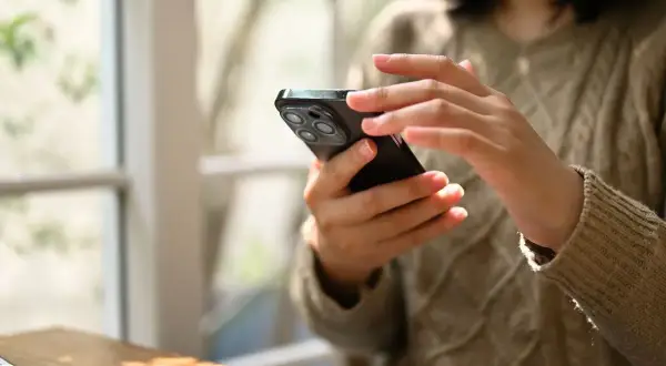 Dłonie kobiety trzymają smartfon, korzystając z aplikacji do zdjęć paszportowych.