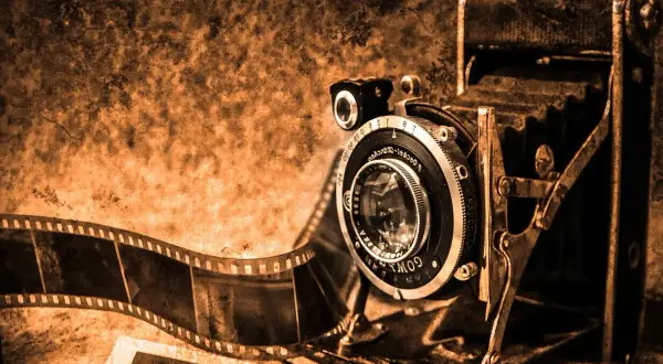 Stary aparat składany i taśma filmowa, symbolizujące historię aparatu fotograficznego.
