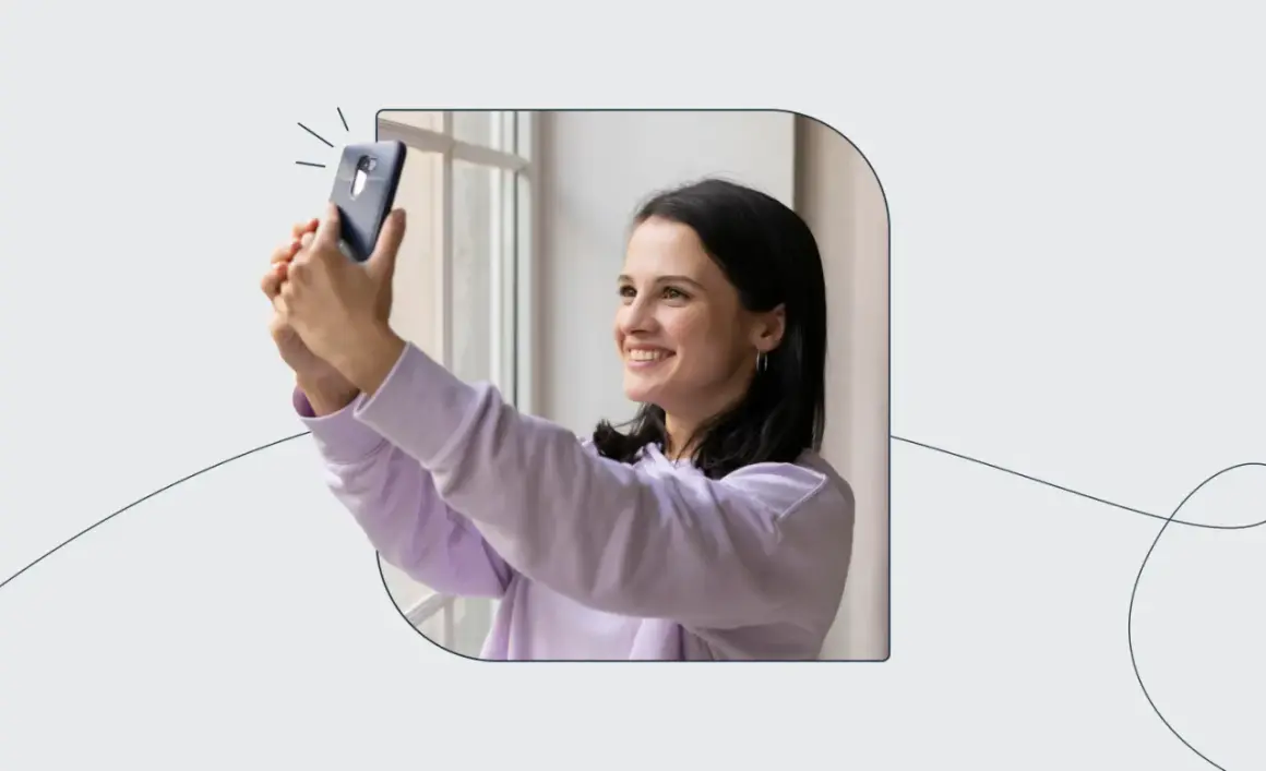 Uśmiechnięta dziewczyna robi selfie telefonem, zastanawiając się, ile zdjęć do dowodu będzie potrzebować.