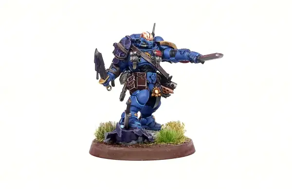 Błękitny Space Marine z mieczem i toporem, gotowy do walki. To zdjęcie na studia, ukazujące szczegóły figurki.